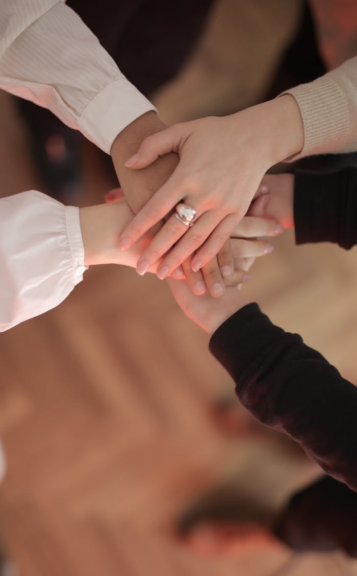 Home Top view of faceless friends in different clothes stacking hands together while standing on wooden floor indoor on sunny day